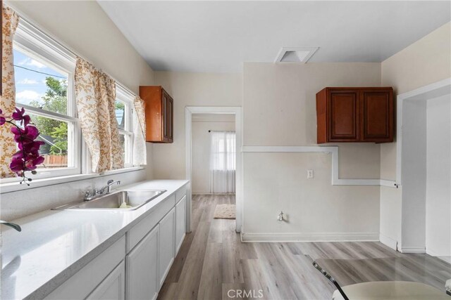 kitchen featuring a sink, light countertops, light wood-type flooring, and baseboards