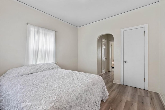 bedroom featuring arched walkways, light wood-style flooring, and baseboards