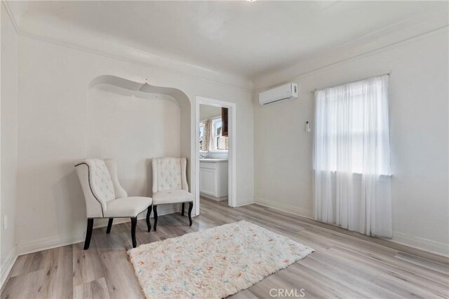 sitting room with a wall mounted air conditioner, wood finished floors, and baseboards