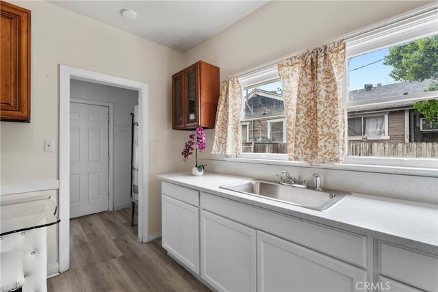 kitchen with a sink, light wood-type flooring, light countertops, glass insert cabinets, and white cabinets
