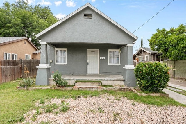 bungalow-style house with a porch, fence, and stucco siding