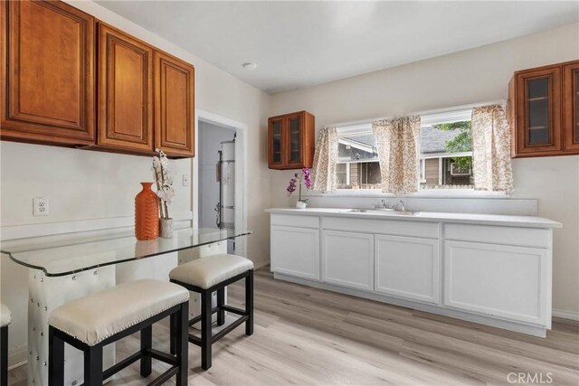 kitchen featuring a sink, glass insert cabinets, light wood-type flooring, and brown cabinets