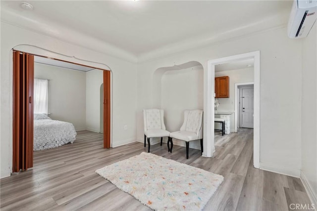 sitting room with light wood-style floors, a wall mounted air conditioner, and baseboards