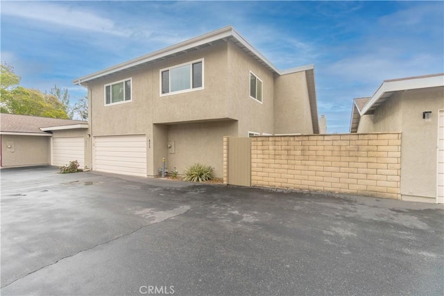 view of side of property featuring stucco siding, a garage, and fence