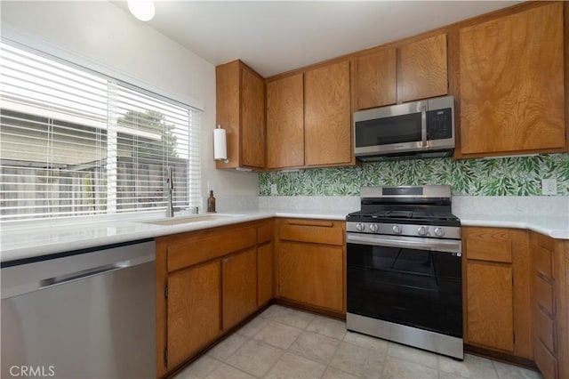 kitchen with stainless steel appliances, a sink, light countertops, and brown cabinets