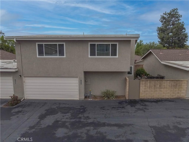 view of front facade with a garage, stucco siding, asphalt driveway, and fence