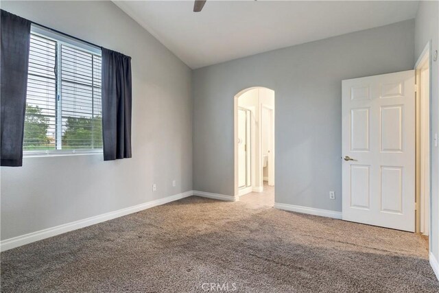 empty room with arched walkways, carpet flooring, baseboards, vaulted ceiling, and a ceiling fan