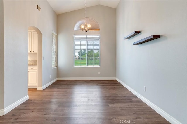 unfurnished dining area featuring dark wood-type flooring, vaulted ceiling, a chandelier, arched walkways, and baseboards