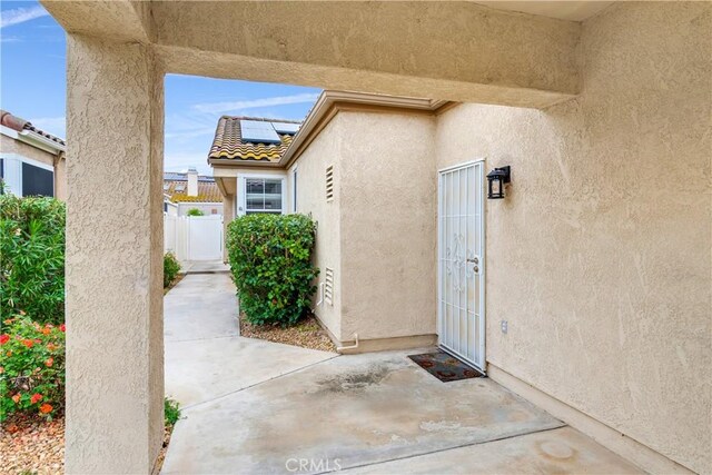 entrance to property with stucco siding, a patio area, fence, and solar panels
