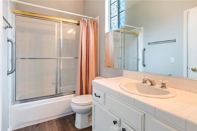 bathroom featuring shower / bath combination with glass door, toilet, vanity, and wood finished floors