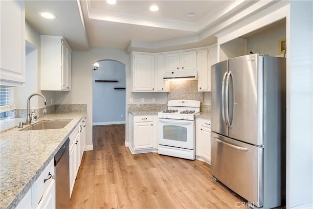kitchen with appliances with stainless steel finishes, a sink, under cabinet range hood, a tray ceiling, and white cabinetry