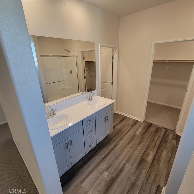 bathroom featuring a stall shower, wood finished floors, double vanity, baseboards, and a spacious closet