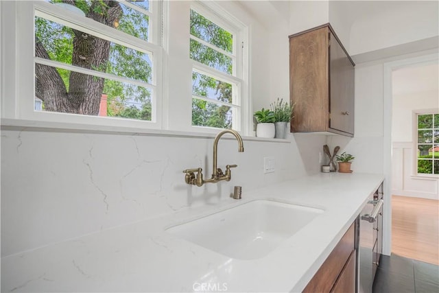 kitchen with a sink, plenty of natural light, brown cabinetry, and dishwasher