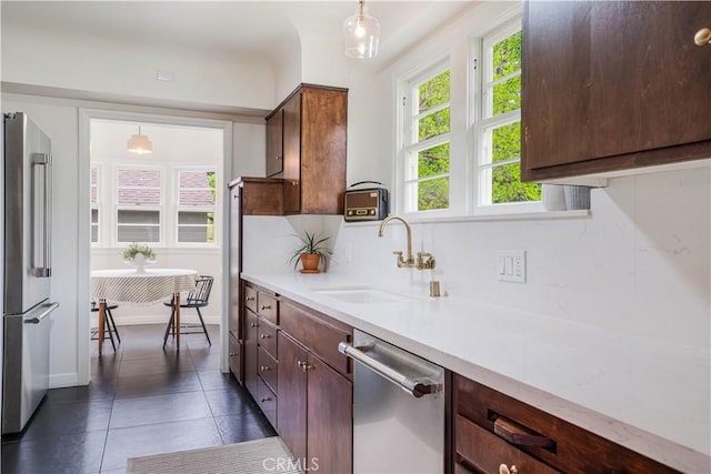 kitchen with stainless steel appliances, a sink, dark tile patterned flooring, and light countertops