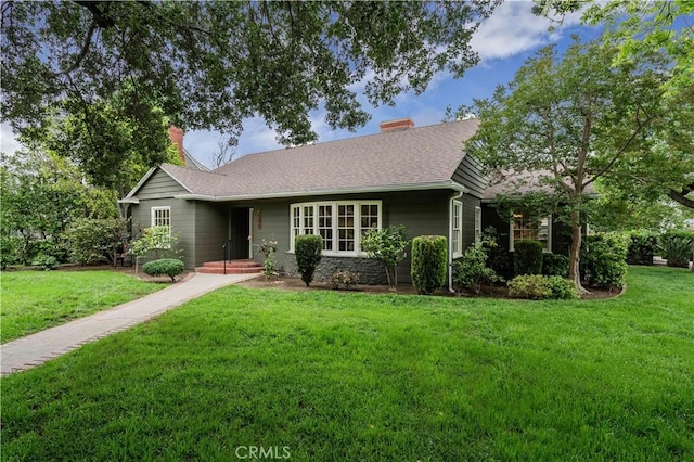 ranch-style home featuring a chimney, a front yard, and a shingled roof