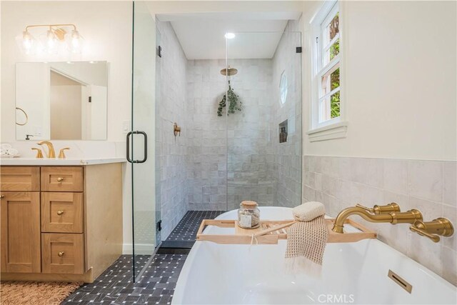 full bath featuring a stall shower, a freestanding tub, vanity, and tile walls
