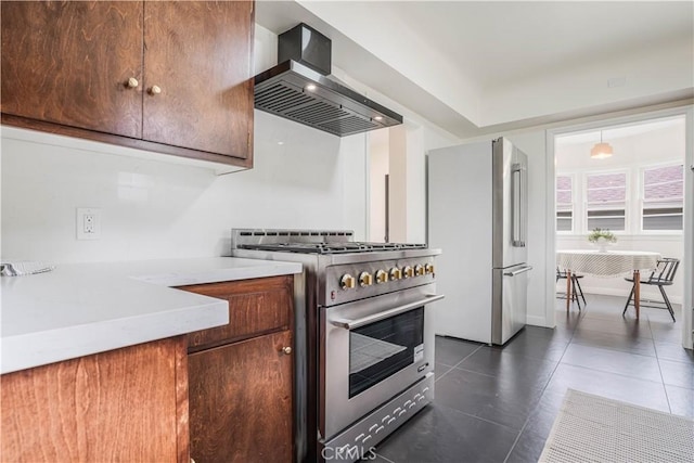 kitchen featuring stainless steel appliances, wall chimney exhaust hood, light countertops, and dark tile patterned flooring