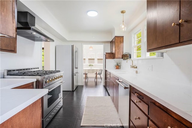kitchen featuring stainless steel appliances, a sink, wall chimney exhaust hood, and light countertops