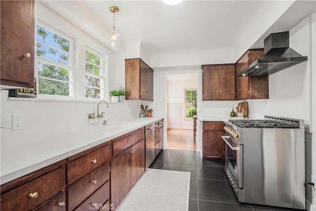kitchen featuring stainless steel appliances, wall chimney range hood, a sink, dark tile patterned flooring, and light countertops