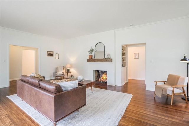 living area with a warm lit fireplace, wood finished floors, ornamental molding, and baseboards