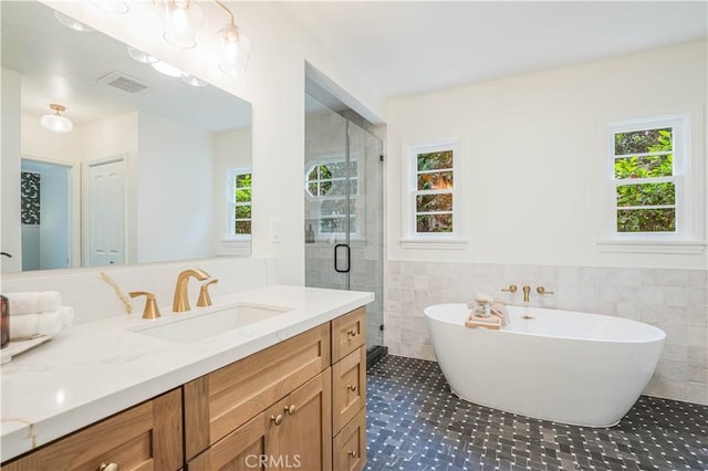 full bathroom featuring tile walls, vanity, a shower stall, a soaking tub, and healthy amount of natural light