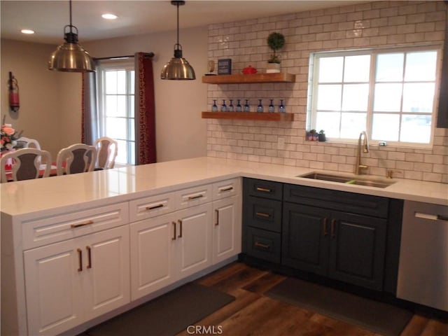 kitchen featuring a peninsula, a sink, light countertops, backsplash, and white cabinets