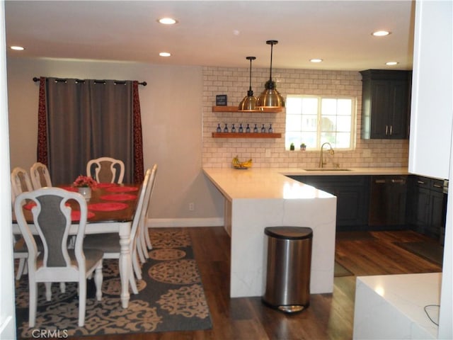 kitchen with a sink, a peninsula, dishwashing machine, light countertops, and dark wood-type flooring
