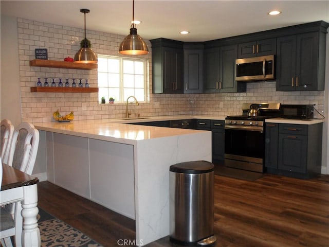 kitchen featuring appliances with stainless steel finishes, a sink, a peninsula, dark wood-style flooring, and decorative backsplash