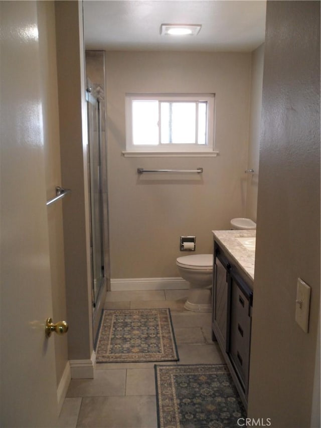 bathroom with vanity, a stall shower, toilet, tile patterned flooring, and baseboards
