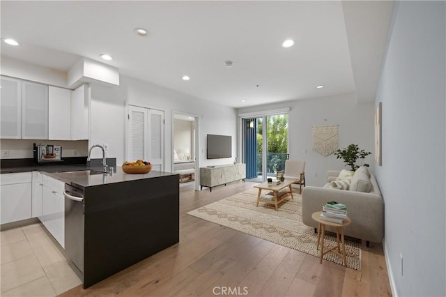 kitchen with a sink, open floor plan, dark countertops, dishwasher, and white cabinets