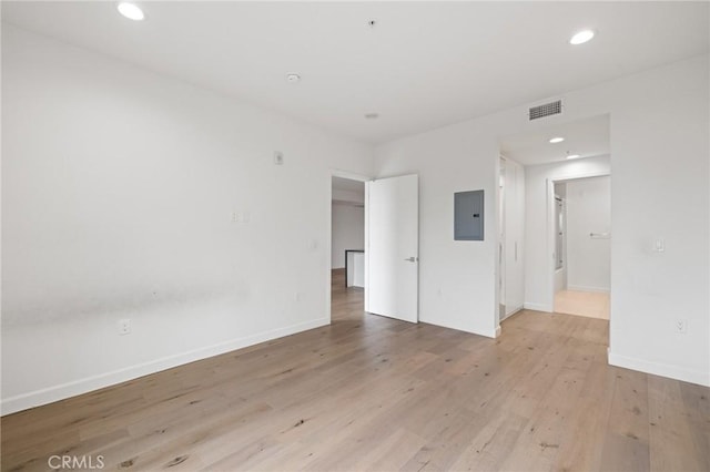 empty room with electric panel, light wood-style flooring, recessed lighting, and baseboards