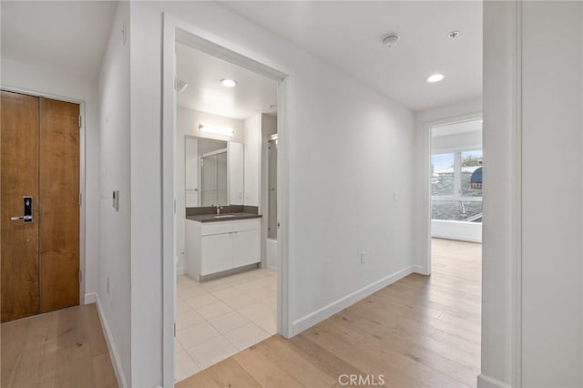 corridor with a sink, light wood finished floors, baseboards, and recessed lighting