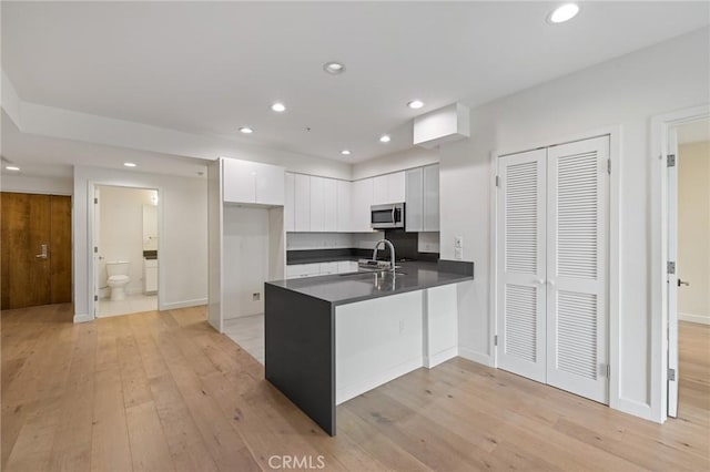 kitchen featuring stainless steel microwave, a peninsula, dark countertops, recessed lighting, and white cabinets