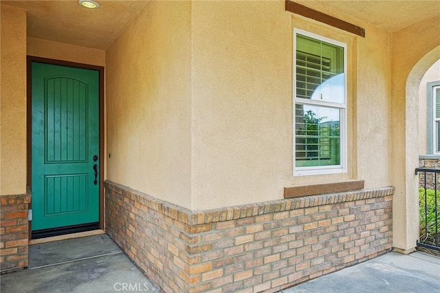 view of exterior entry with stucco siding and brick siding