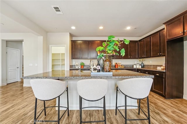 kitchen with light wood-style flooring, a kitchen bar, a kitchen island with sink, baseboards, and recessed lighting