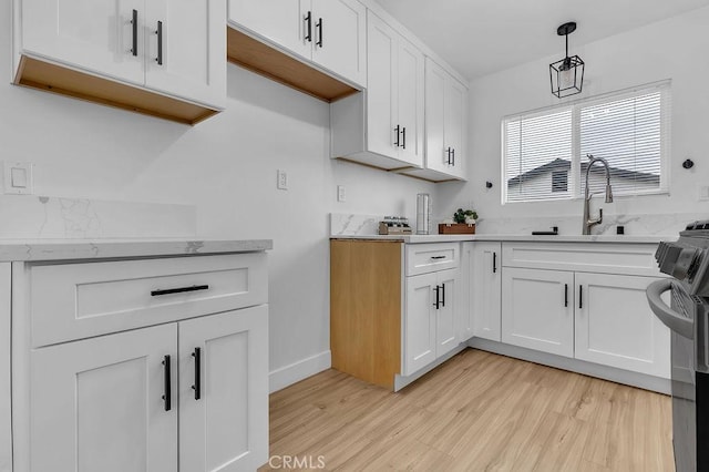 kitchen featuring light wood-style floors, a sink, white cabinets, and decorative light fixtures