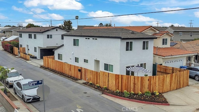 view of side of property featuring fence, a residential view, stucco siding, and a garage