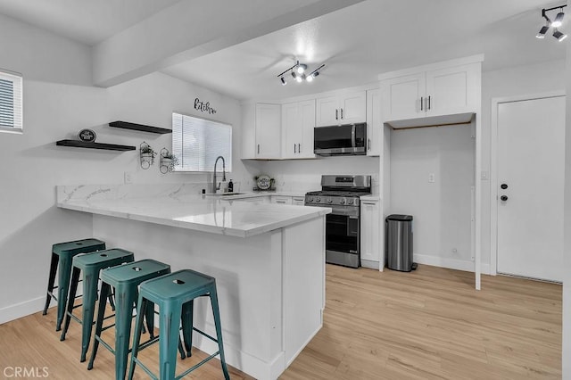 kitchen featuring appliances with stainless steel finishes, a sink, white cabinetry, a kitchen breakfast bar, and a peninsula