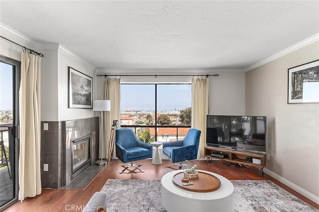 living area with wood finished floors, a tile fireplace, ornamental molding, and baseboards