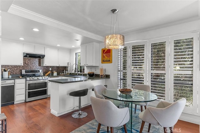 kitchen featuring range with two ovens, under cabinet range hood, a peninsula, dark countertops, and white cabinetry