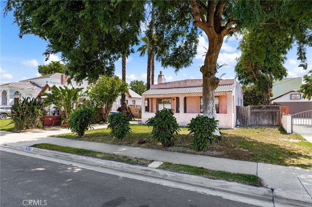 view of front of house featuring a tiled roof, fence, a chimney, stucco siding, and a gate