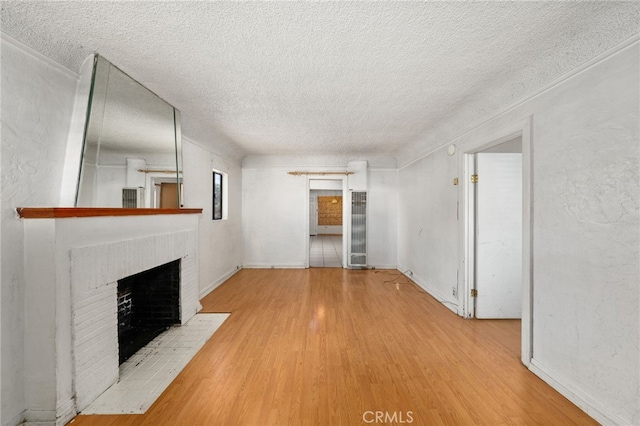 unfurnished living room featuring wood finished floors, a textured ceiling, a brick fireplace, and baseboards