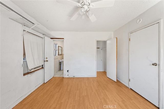 unfurnished bedroom featuring wood finished floors, a textured ceiling, a closet, ensuite bathroom, and ceiling fan