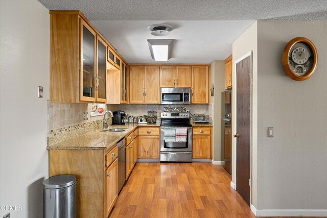 1037 Cortina Ct, Orland, CA 95963 - kitchen featuring stainless steel appliances, a sink, light wood finished floors, light stone countertops, and decorative backsplash