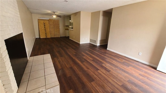 unfurnished room featuring ceiling fan, wood finished floors, a textured ceiling, a brick fireplace, and baseboards