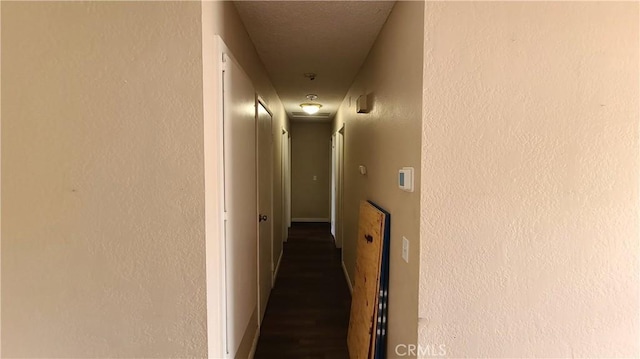 corridor featuring baseboards and a textured wall