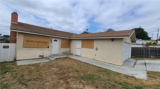 rear view of house with fence, a garage, stucco siding, and a chimney