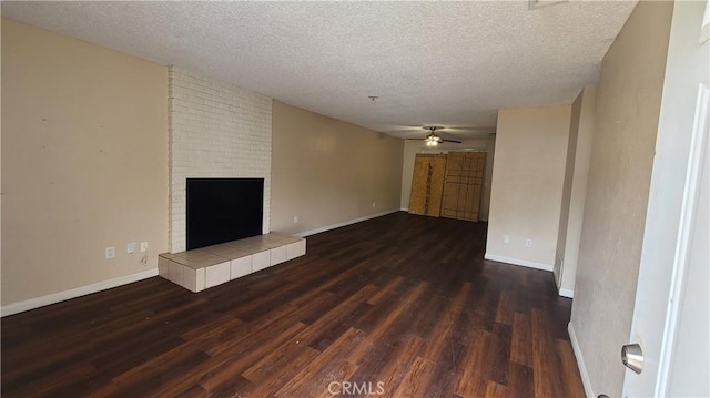unfurnished living room with dark wood-type flooring, a textured ceiling, a ceiling fan, a tiled fireplace, and baseboards