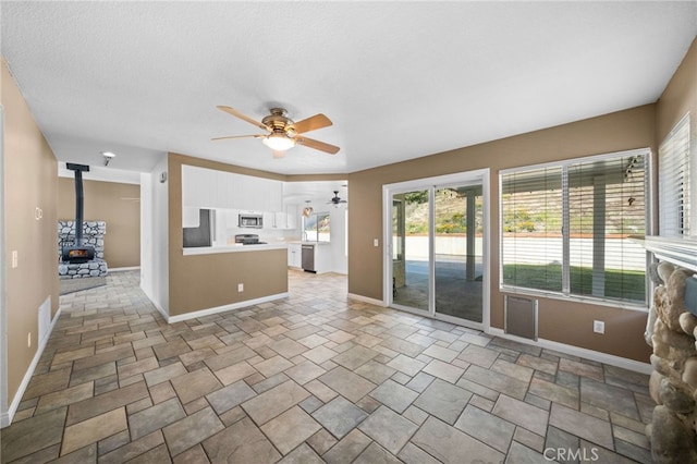 39812 Barcelona, Murrieta, CA 92562 - unfurnished living room featuring a ceiling fan, healthy amount of natural light, a wood stove, and baseboards
