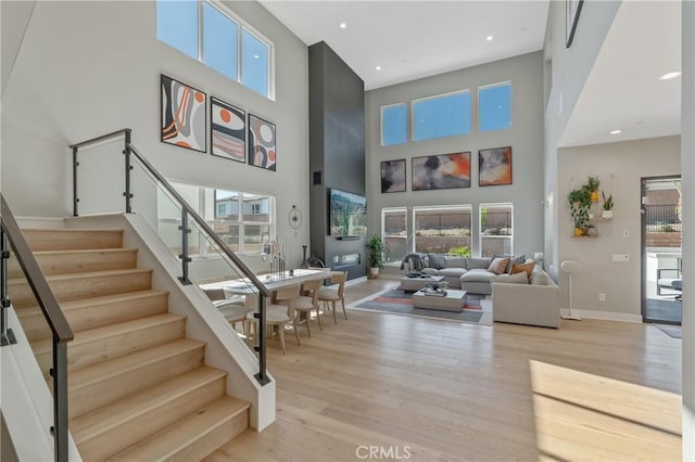 living area with a high ceiling, light wood-style floors, stairway, healthy amount of natural light, and recessed lighting